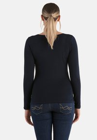 Marineblaues Langarmoberteil mit Rundhalsausschnitt, taillierter Form und glatter Textur, kombiniert mit dunklen Jeans mit dekorativer Taschennaht.