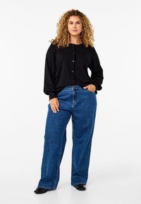 Schwarze Knopf-Cardigan mit langen Ärmeln, kombiniert mit hochgeschnittenen, lockeren blauen Jeans. Glatte Textur, klassisches Design.