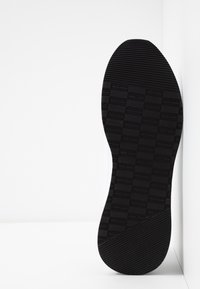 Podeszwa buta z teksturowanym czarnym gumowym wzorem, z poziomym układem prostokątów i rowków zapewniającym przyczepność i trakację.