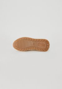 Semelle en caoutchouc avec texture antidérapante, de couleur brune et profonde rainures pour une meilleure traction. Logo de la marque embossé et finition lisse.