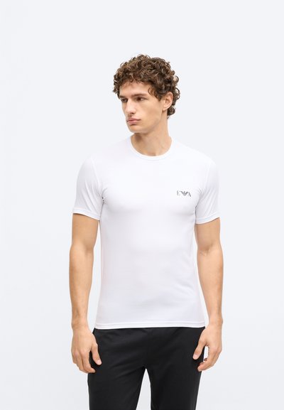 Balta īsroku t-krekls no gludas auduma, ar apaļu kaklu un mazu melnu logotipu kreisajā krūtīs. Vienkāršs un pieguļošs dizains.