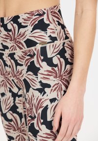 Leggings taille haute avec un motif floral, présentant des fleurs bordeaux et crème sur un fond marine foncé. Tissu lisse et extensible avec une étiquette de logo.