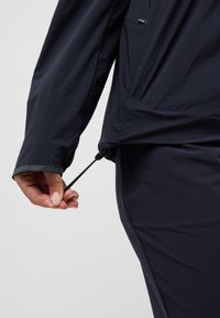 Giacca leggera blu navy con maniche lunghe, dotata di regolazione con cordoncino all'orlo e di una tasca laterale con zip.