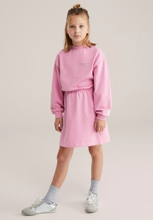 Rózsaszín pulóverruha, laza szabással, hosszú ujjal, húzott derékkal és finom hímzett részlettel. Szürke zoknival és ezüst cipővel párosítva.