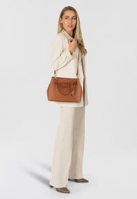 Borsa a mano in pelle color cuoio con logo impresso, doppi manici e tracolla removibile. Presenta hardware lucido e una silhouette strutturata.
