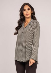 Chemise boutonnière à motif noir et blanc avec col, manches longues et un ourlet légèrement asymétrique. Tissu lisse avec une texture douce.