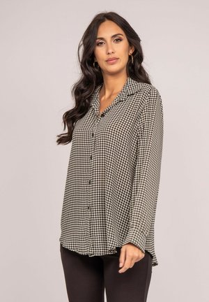 Chemise boutonnière à motif noir et blanc avec col, manches longues et un ourlet légèrement asymétrique. Tissu lisse avec une texture douce.
