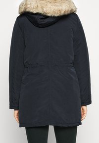 Navy blue parka with a faux fur-lined hood, drawstring waist, and long sleeves. Smooth texture, knee-length design, and hidden pockets.