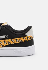 Svart sneakers med gul leopardmönster sidremsa och vit sula. PUMA-logotyp på sidan, vadderad krage och strukturerad tygöverdel.
