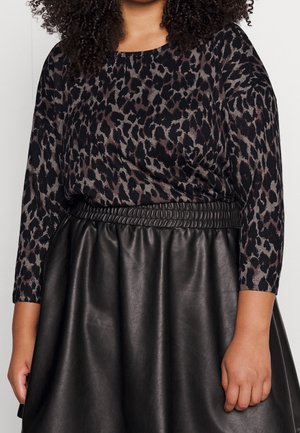 Femme portant un haut à manches longues noir et gris imprimé léopard, rentré dans une jupe en cuir noire taille haute avec une ceinture froncée.