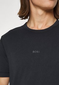 T-shirt de algodão preto com decote redondo, mangas curtas e um logo "BOSS" em tom sobre tom na frente, apresentando detalhes de costura sutis.