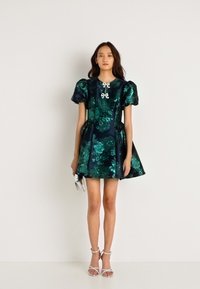 Σαφράν πράσινο φλοράλ φόρεμα με φουσκωτά μανίκια, σατέν υφή, εφαρμοστό κορσέ, φουσκωτή φούστα και φιόγκο στη λαιμόκοψη. Συνδυάζεται με λουράκια σε τακούνια.