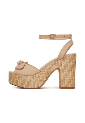 Beżowe sandały na platformie z plecionym korkowym obcasem, regulowanym paskiem wokół kostki oraz kokardą na pasku przy palcach. Wierzch z fakturowanej tkaniny.