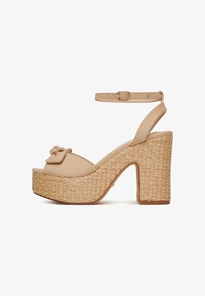 Smėlio spalvos platforminės basutės su pintu šiaudiniu kulnu, reguliuojamu čiurnos dirželiu ir kaspinėliu ant pirštų dirželio. Tekstūruota audinio viršutinė dalis.