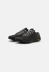 Scarpe nere in suede con lacci grigi, profilo basso, suola in gomma testurizzata e logo Vibram. Superficie liscia con accenti modellati e design curvo.