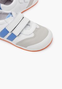 Sneaker bianche e grigie con accentuazioni blu e cinturini in velcro. Presentano una suola in gomma testurizzata con un bordo arancione, che migliora la presa e lo stile.