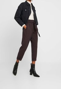 Schwarze Jeansjacke über einem weißen, gerippten Oberteil, kombiniert mit karierter, hochtaillierter Hose und schwarzen Ankle Boots mit Blockabsatz.