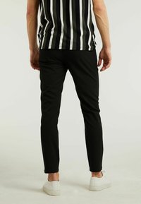 Zwarte slim-fit broek met een gladde textuur, gecombineerd met witte sneakers. De top heeft verticale zwart-witte strepen.