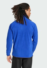 Blue fleece jacket with a high collar, long sleeves, and a smooth texture. Features a plain design and a slightly longer back hem.