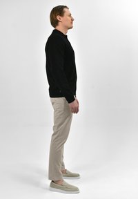 Zwarte lange mouw polo, beige op maat gemaakte broek en lichtgroene instapschoenen. Eenvoudig design, effen kleuren en gladde texturen.