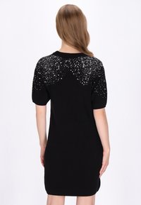 Fekete kötött ruha rövid ujjakkal, csillogó gyöngyökkel díszítve a vállrészen, sima textúrával és testhezálló siluettel.