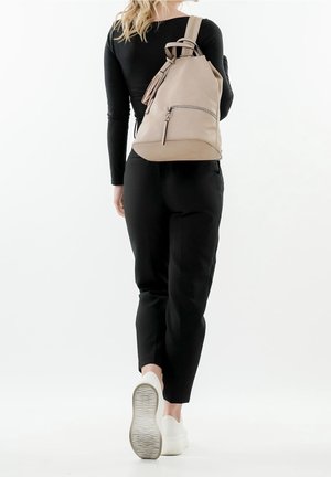 Beige nahkareppu, jossa on nyörikirettävä sulku, sivuvetoketjullinen tasku ja tupsukoriste, käytetty yhdellä olalla. Mustat vaatteet ja valkoiset kengät.