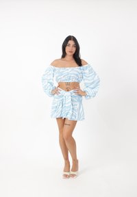 Blaue und weiße gemusterte Schulterfreie Crop-Top mit Puffärmeln, kombiniert mit einem passenden, schwingenden Minirock und gebundenem Taillendetail.