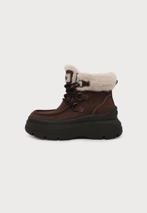 Bottine d'hiver marron à la cheville avec semelle épaisse noire, lacets noirs, et col et languette doublés en fausse fourrure blanche.