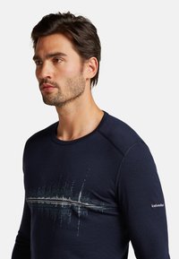 Marineblauwe longsleeve shirt van ademend materiaal met een geluidsgolf graphic in lichtere tinten over de borst en een logo op de mouw.