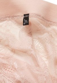 Lingerie di un rosa chiaro con sovrapposizione di pizzo, dotata di un'etichetta nera. Il tessuto è morbido, liscio e semi-trasparente in alcune parti.
