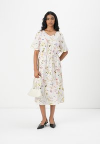 Blomsterprint kjole med korte ærmer, V-hals, indsnævret talje og en svævende silhuet. Sammen med en hvid håndtaske og sorte hæle.