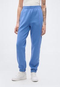 Φόρμα σε ανοιχτό μπλε χρώμα, κατασκευασμένη από απαλό ύφασμα, με ελαστική μέση και μανσέτες, πλαϊνές τσέπες και άνετη εφαρμογή.