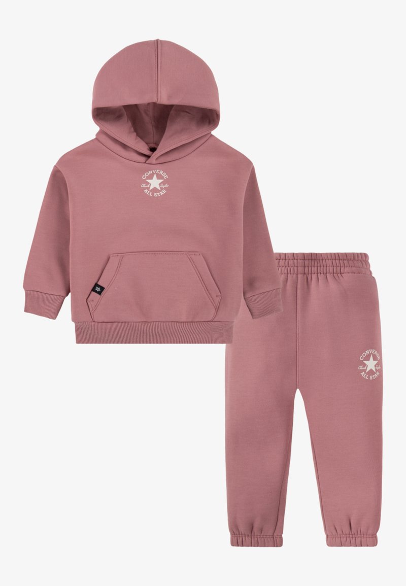 Sweat à capuche en coton rose avec une poche kangourou et un logo blanc, associé à un pantalon fuselé assorti avec une ceinture élastique.