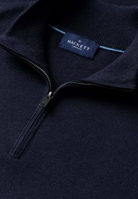 Tmavě modrý svetr se stojáčkem na zip do čtvrtiny, žebrovaným límcem a štítkem "Hackett London" uvnitř výstřihu.