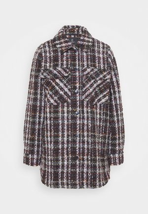 Veste en plaid tissée dans des rouges foncés, des noirs et des blancs. Comprend deux poches poitrine, un devant à boutons et un col arrondi. Tissu texturé.
