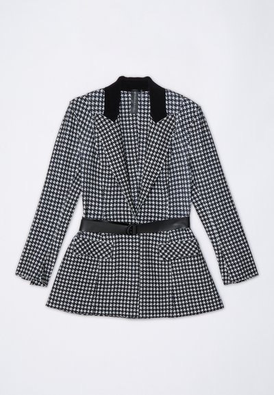Fekete-fehér houndstooth mintás zakó fekete bársony gallérral, övvel a deréknál és két elülső zsebbel. Testre szabott dizájn, hosszú ujjak.