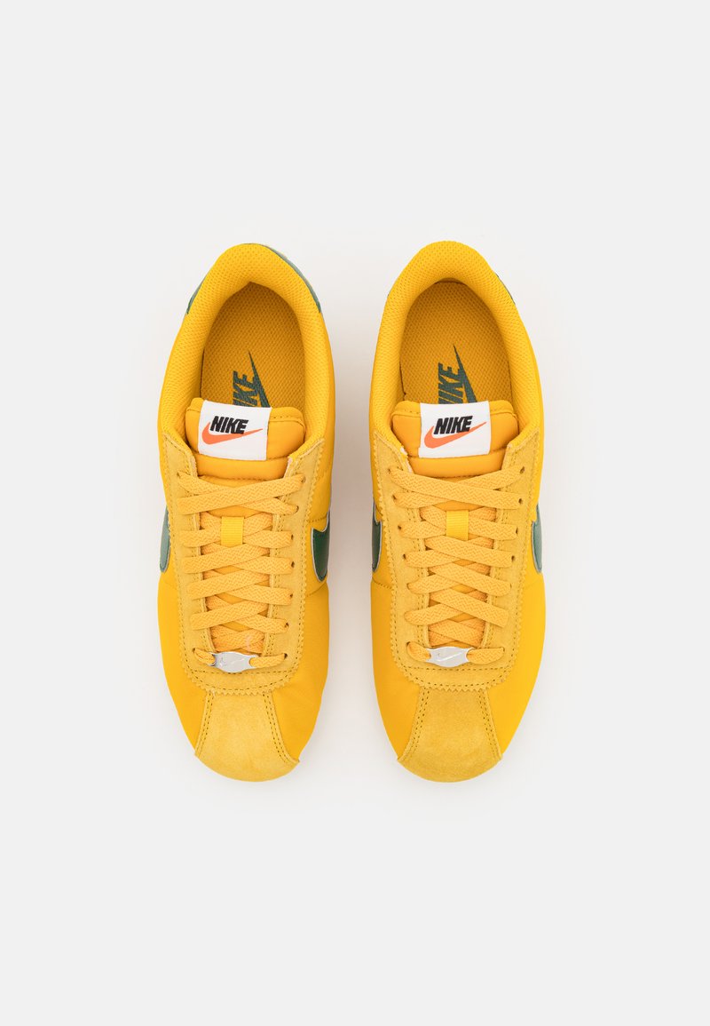 Zapatillas Nike amarillas con acentos verdes, malla texturizada y materiales de ante, cordones planos y un logo blanco en la lengüeta.