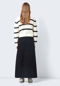 Svart denim maxi skirt med høy midje og baklommer, sammen med en kremfarget genser med svarte horisontale striper.