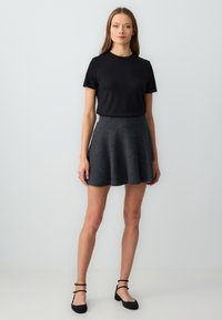 Zwarte ribbelige shirt met korte mouwen gecombineerd met een uitlopende, donkergrijze rok. De rok heeft een gladde textuur en eindigt boven de knie. Zwarte platte schoenen.