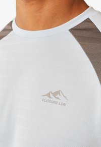 T-shirt de sport à manches courtes bleu clair avec des rayures texturées, des accents gris aux épaules et un logo imprimé portant la mention "CLOSURE LDN."
