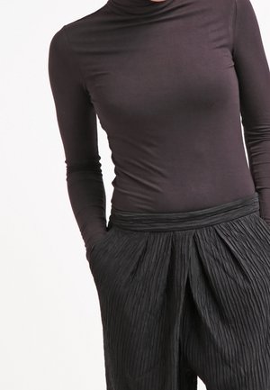 Black long-sleeve turtleneck top paired with high-waisted black pleated trousers, featuring a textured fabric and relaxed fit.