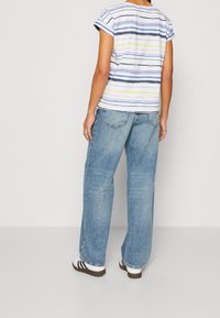 Pruhovaná košile s krátkým rukávem v modré a bílé barvě, se žlutými akcenty; spárovaná se světle modrými širokými džíny a černobílými teniskami.