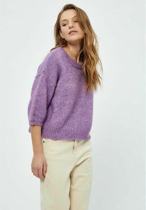 Lilla strikket sweater med korte ærmer, ribbet halsudskæring og kant. Det strukturerede garn tilføjer blødhed, parret med lyse bukser.