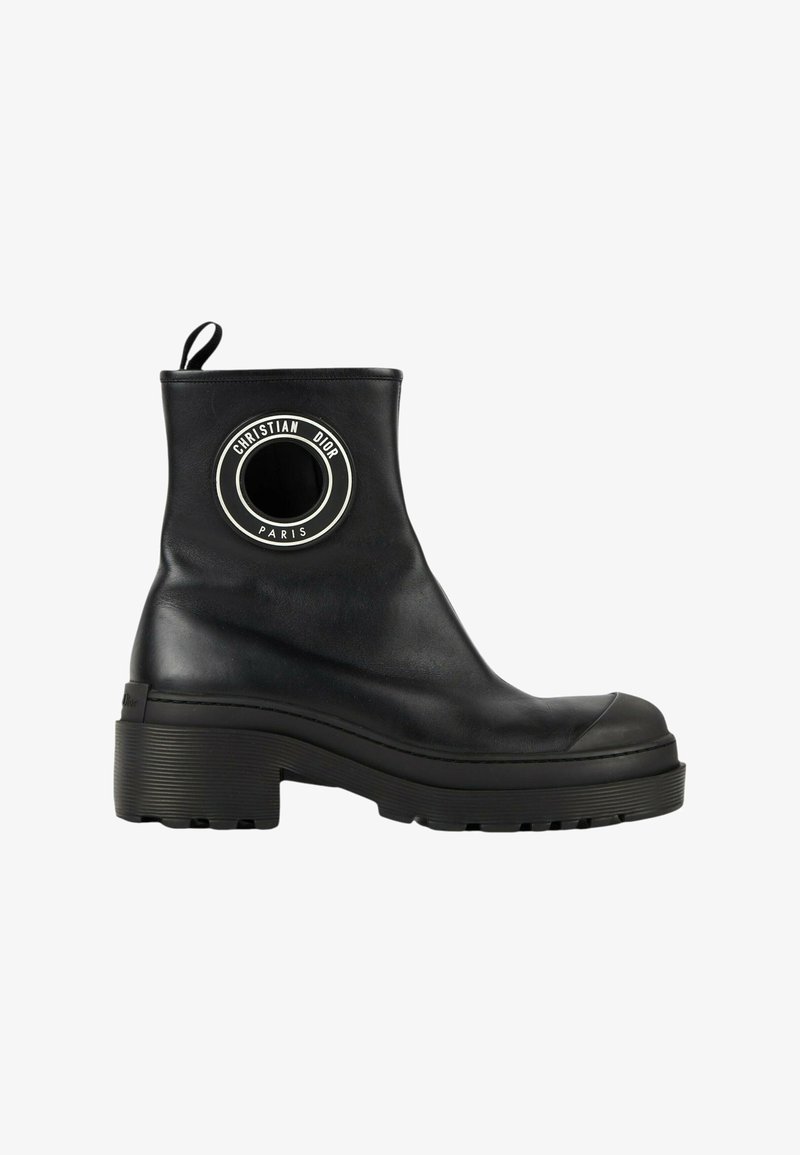 Bottine en cuir noir avec semelle épaisse et écusson rond portant le logo "Christian Dior Paris" sur le côté.