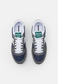 Marineblå og grå Saucony Jazz joggesko har overdel i mesh og suede, hvite snøringer og grønne merkeetiketter på tungen. Flate gummisåler.