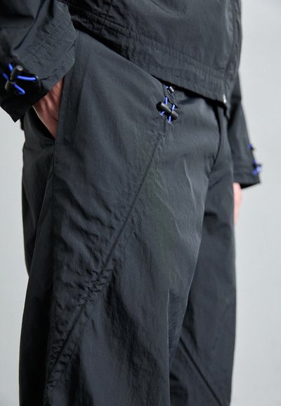 Black windbreaker with a textured finish, featuring blue accents on the hardware and stitching. Includes side pockets and a fitted design.
