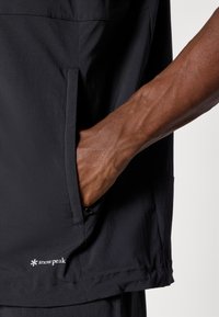 Black lightweight shirt with a side pocket. Features smooth texture, clean lines, and Snow Peak logo on the hem.