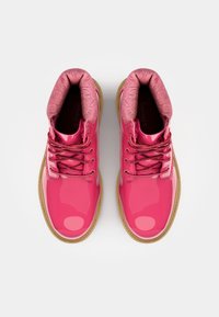 Botas de couro patentado rosa com um colarinho texturizado em rosa, atacadores redondos e uma sola de borracha bege. Apresenta padrões florais em relevo no colarinho.