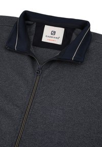 Giacca zip-up grigia scura con tessuto testurizzato, colletto in rete blu navy e un'etichetta con la scritta "GABBIANO" in taglia media. Presenta una cerniera a contrasto.
