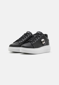 Schwarze Leder-Sneaker mit weißen Gummisohlen, die ein Schnürdesign und eine Cartoonfigur-Akzent an der Seite aufweisen.